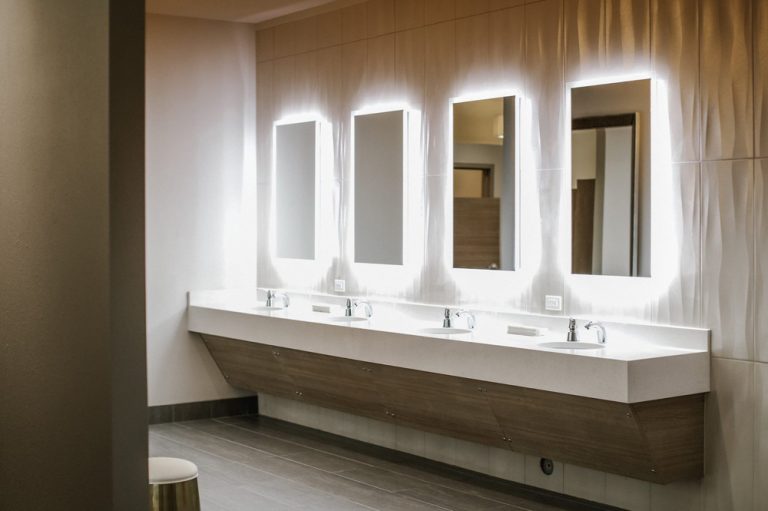 Luxurious design of women's locker room, showing 4 backlit mirrors and white vanity.