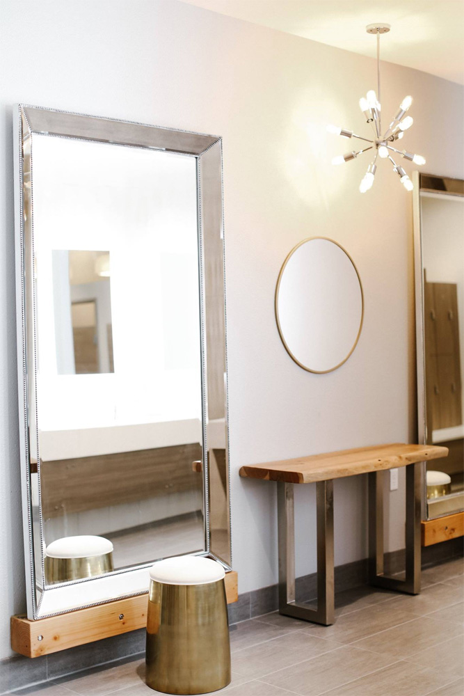 Large silver mirror with brass stool and stylish light in women's locker room.
