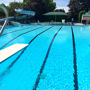 Vibrant blue waters and painted lap lanes in crystal clear outdoor pool, with diving board and safety rails.