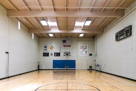 Empty gym with basketball court, various signs and score clock.