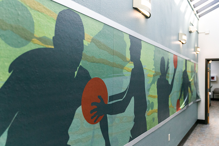 green and blue mural of sports figures playing with orange ball. Mural lines open hallway.