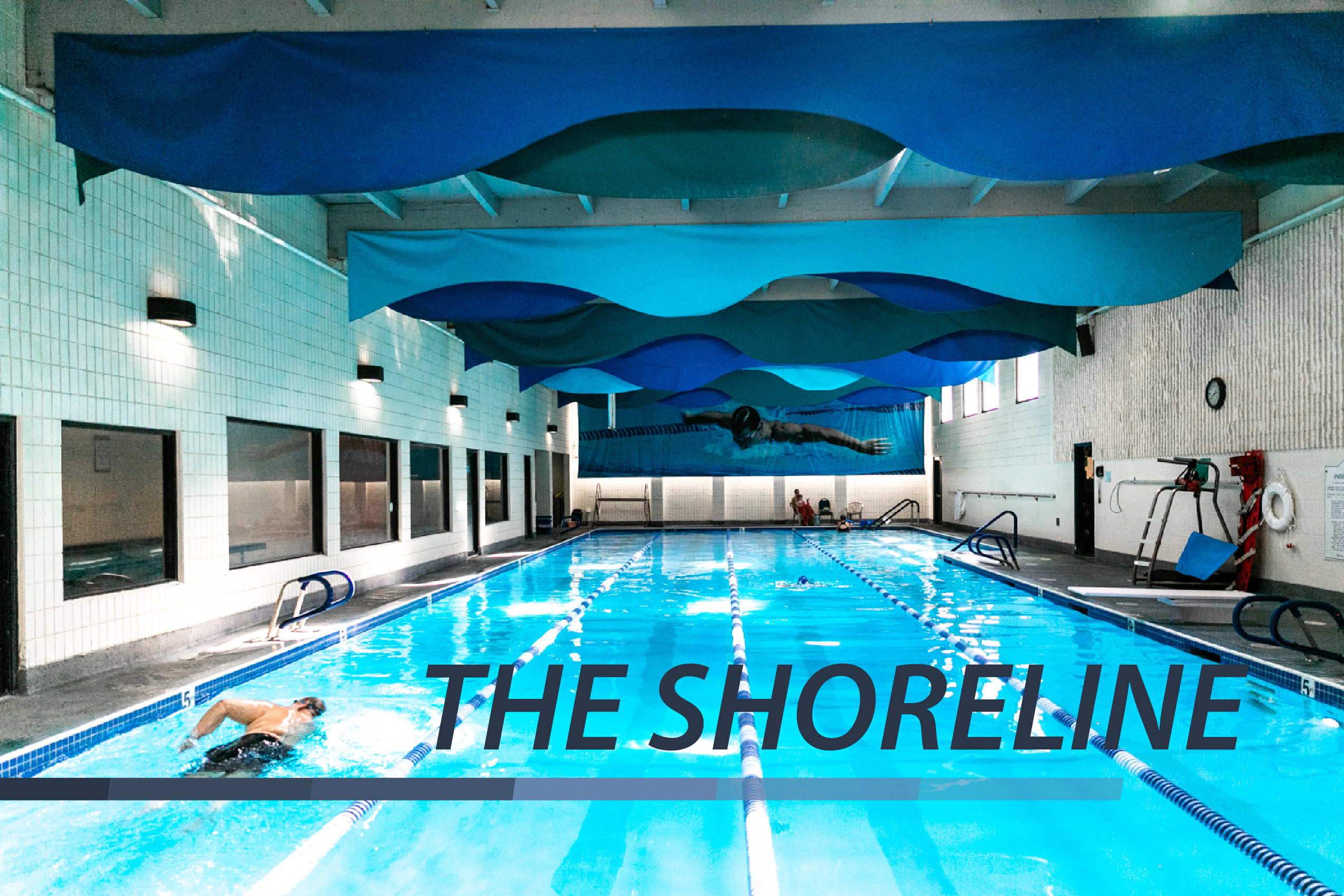 Indoor pool with vibrant blue colors and text on photo saying "The Shoreline."