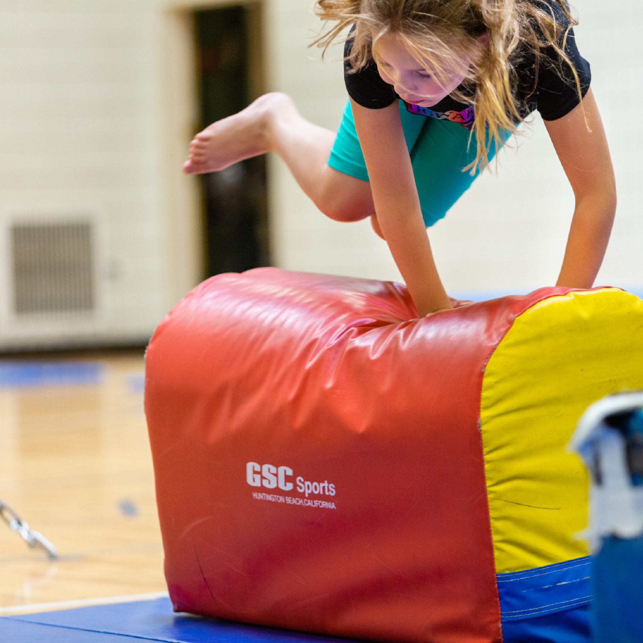 Young girl joyfully jumping over colorful obstacle while participating in Fit Kids fitness program.
