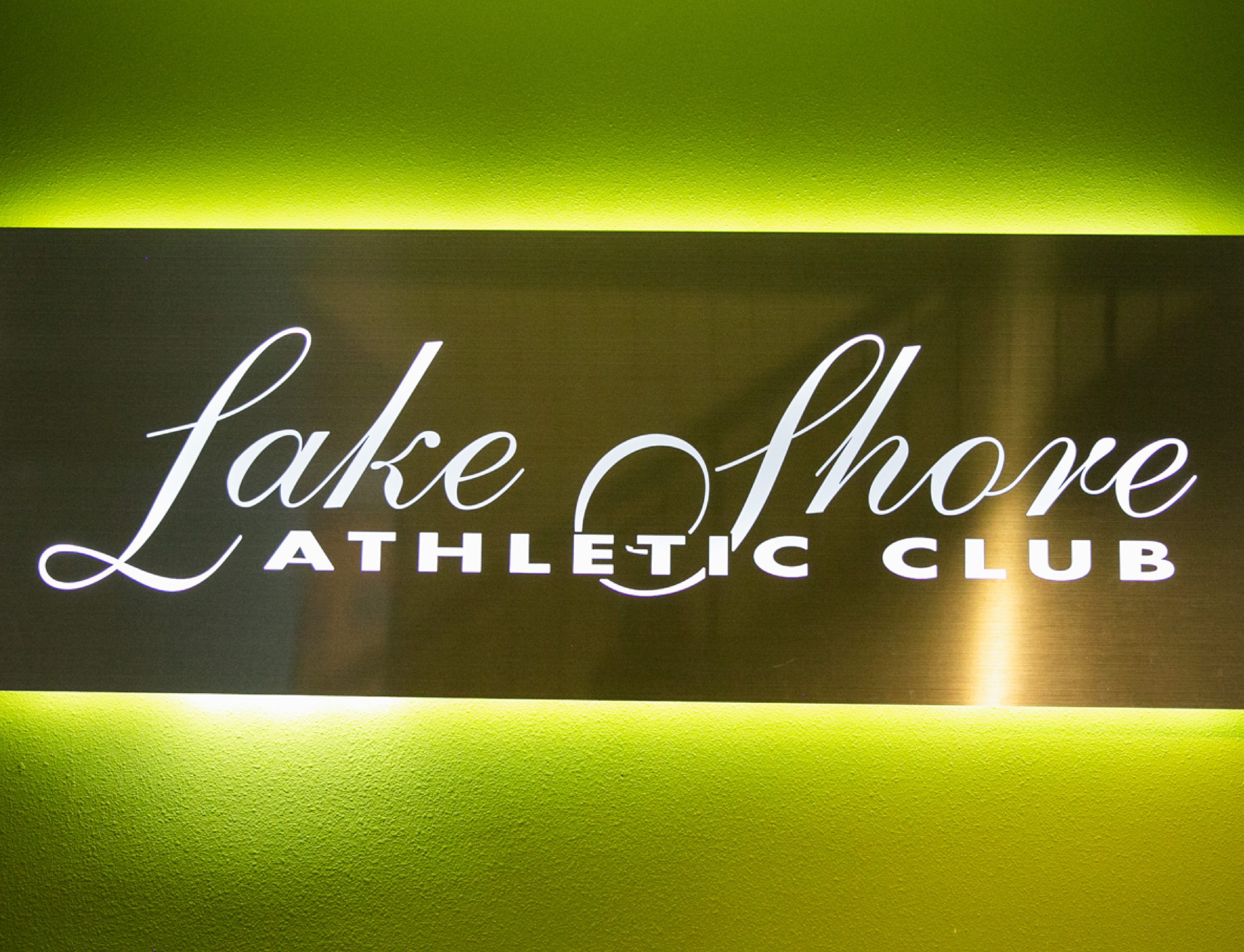 Backlit steel sign with Lake Shore Athletic Club logo, against a lime green painted wall.